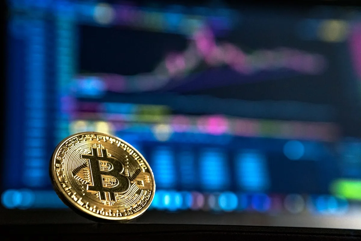 Physical Bitcoin gold coin in front of crypto trading charts — cryptocurrency investment in India